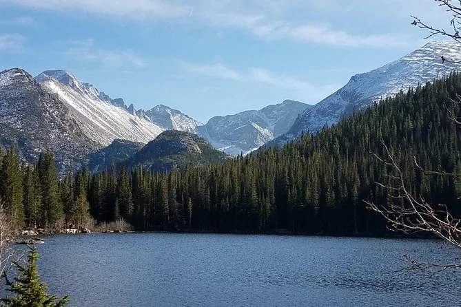 Ein von Wald umgebener Bergsee unterhalb schneebedeckter Granitgipfel