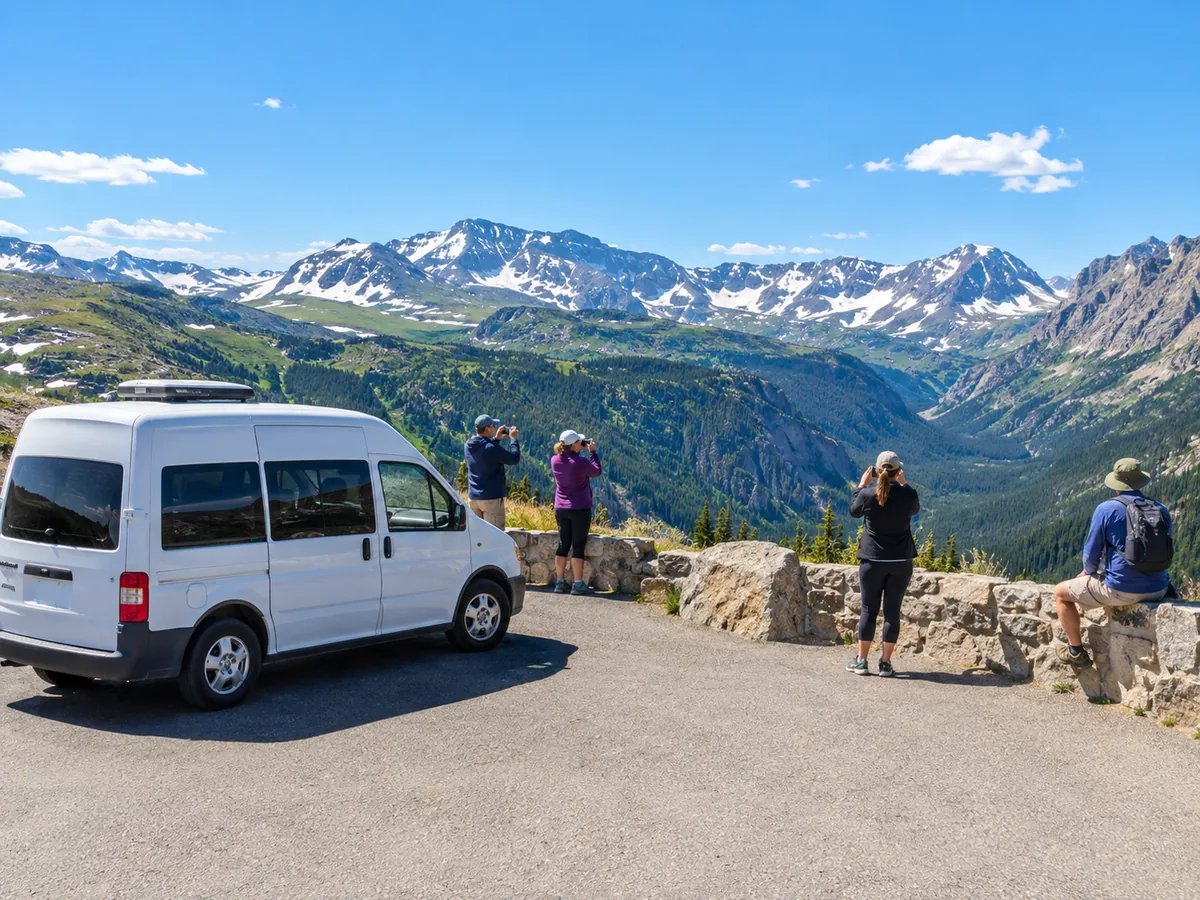 Ein weißer Touring-Van steht an einem Steinaussichtspunkt oberhalb der Baumgrenze, Besucher fotografieren schneebedeckte Gipfel